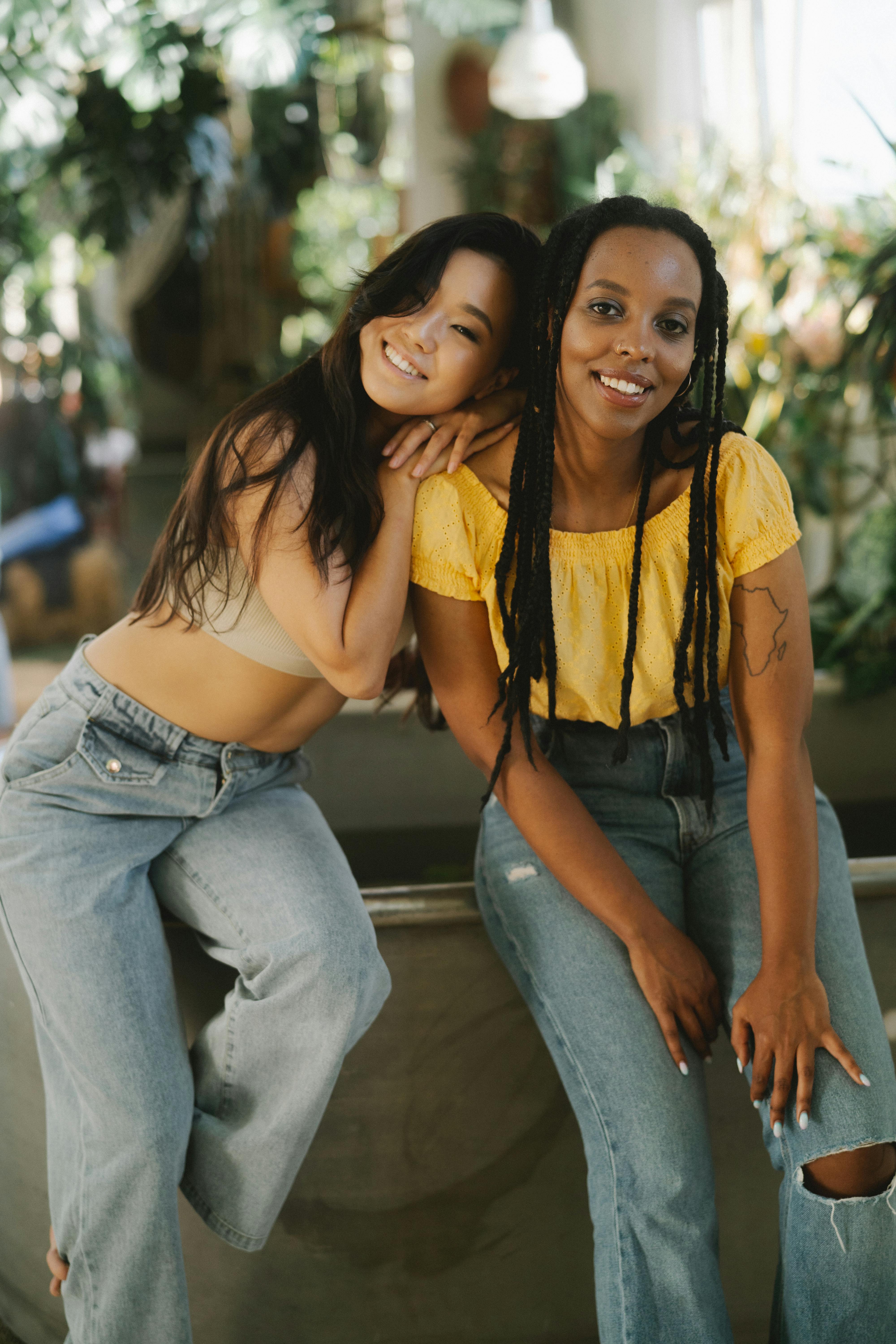Two smiling friends embracing, surrounded by greenery in a bright indoor space, radiating warmth and friendship.