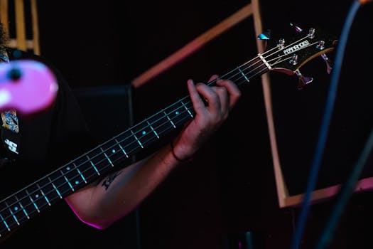 A detailed view of a musician playing a bass guitar on stage, showcasing finger technique.