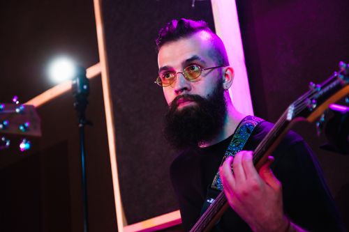 Free A bearded musician plays an electric guitar in a dimly lit indoor music studio. Stock Photo
