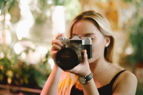 Free Young woman using vintage camera in a sunny outdoor setting, capturing a moment. Stock Photo