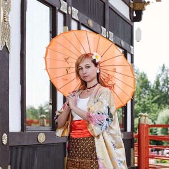 Woman wearing a vibrant kimono poses with a Japanese paper umbrella outdoors.（イメージ）