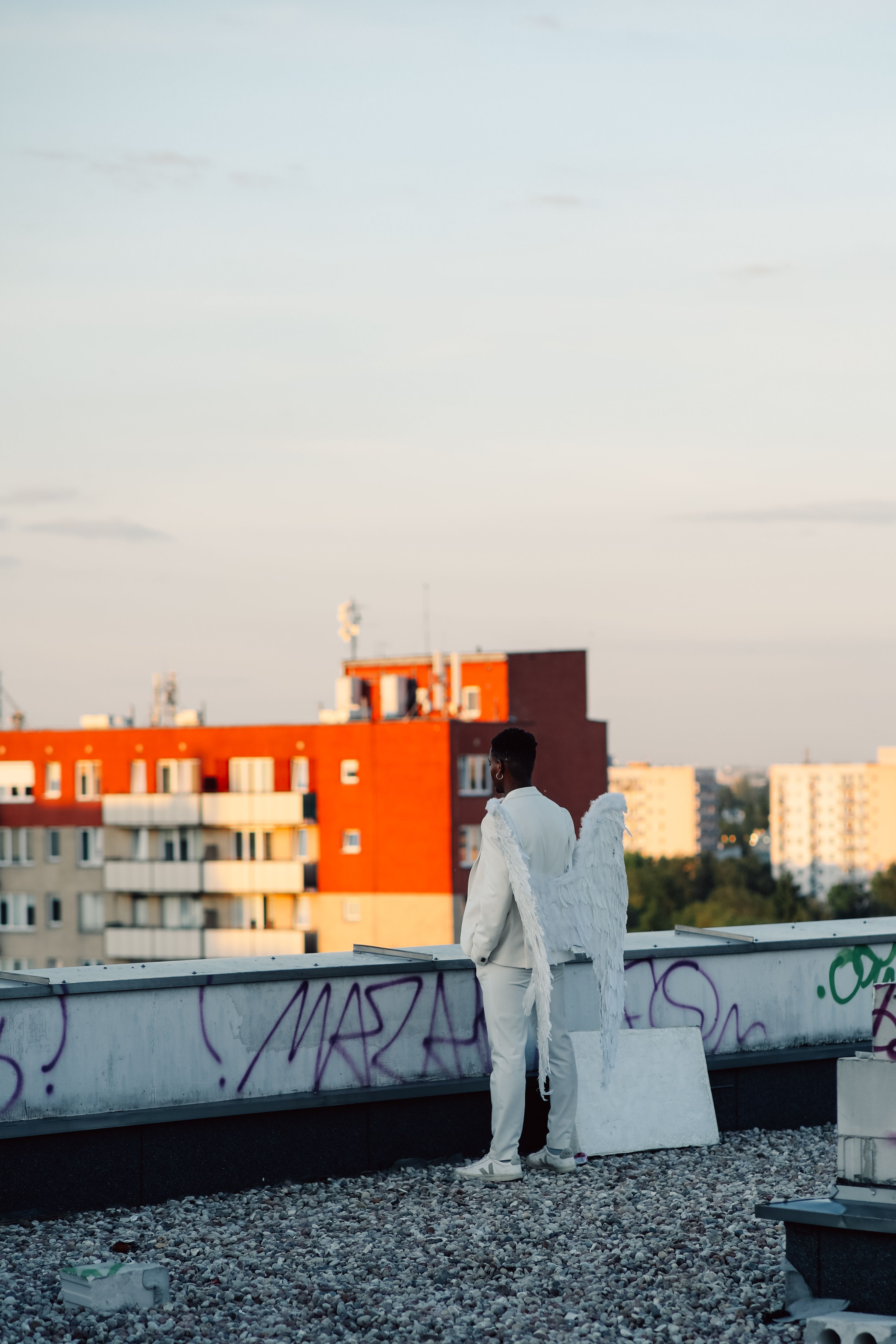 Man dressed as an angel with wings standing on a city rooftop, contemplating the view.
