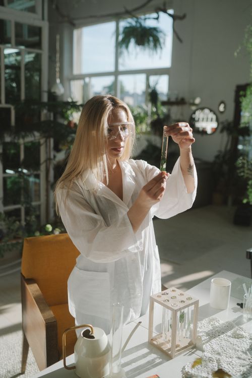 Free A young woman in a laboratory examines a test tube surrounded by natural lighting and plants. Stock Photo