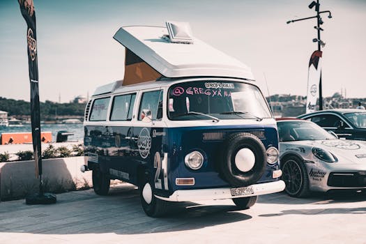 Vintage van showcased at an outdoor car rally beside a modern sports car on a sunny day.