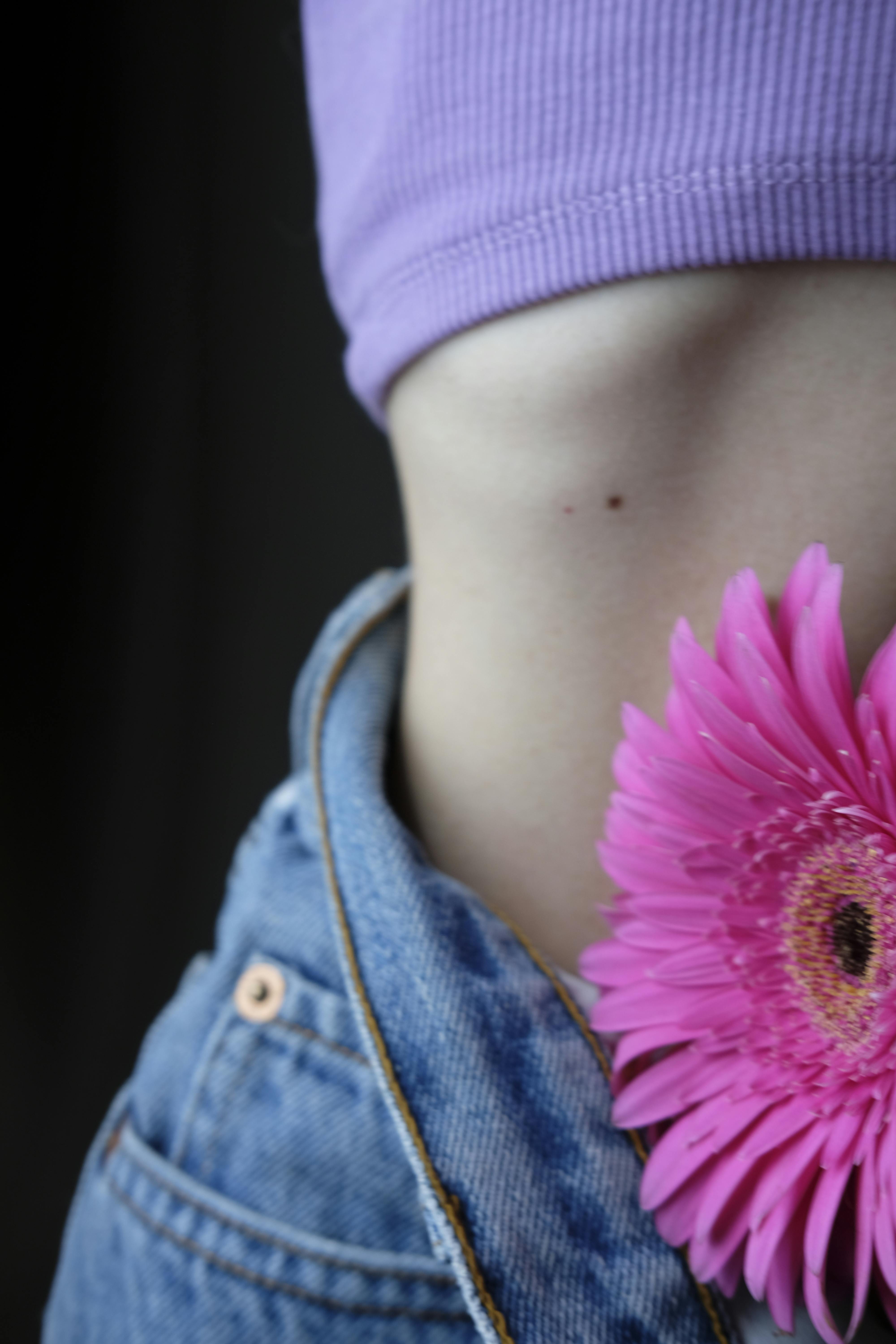 Close-up shot featuring blue denim, pink flower, and exposed midriff with a purple top.