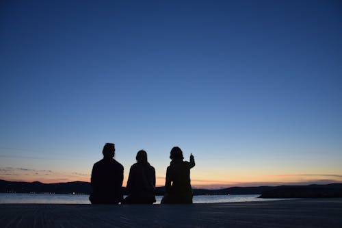 A Silhouette of People Sitting Near the Lake