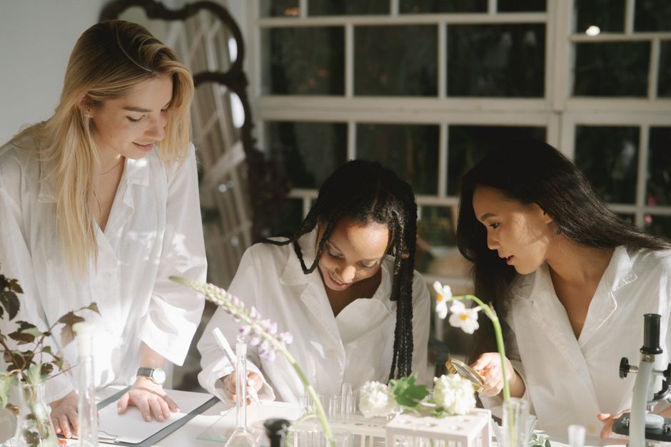 Three women scientists collaborate in a bright, plant-filled laboratory.