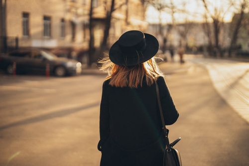 Free A woman in a black coat and hat walking on a city street during sunset. Stock Photo