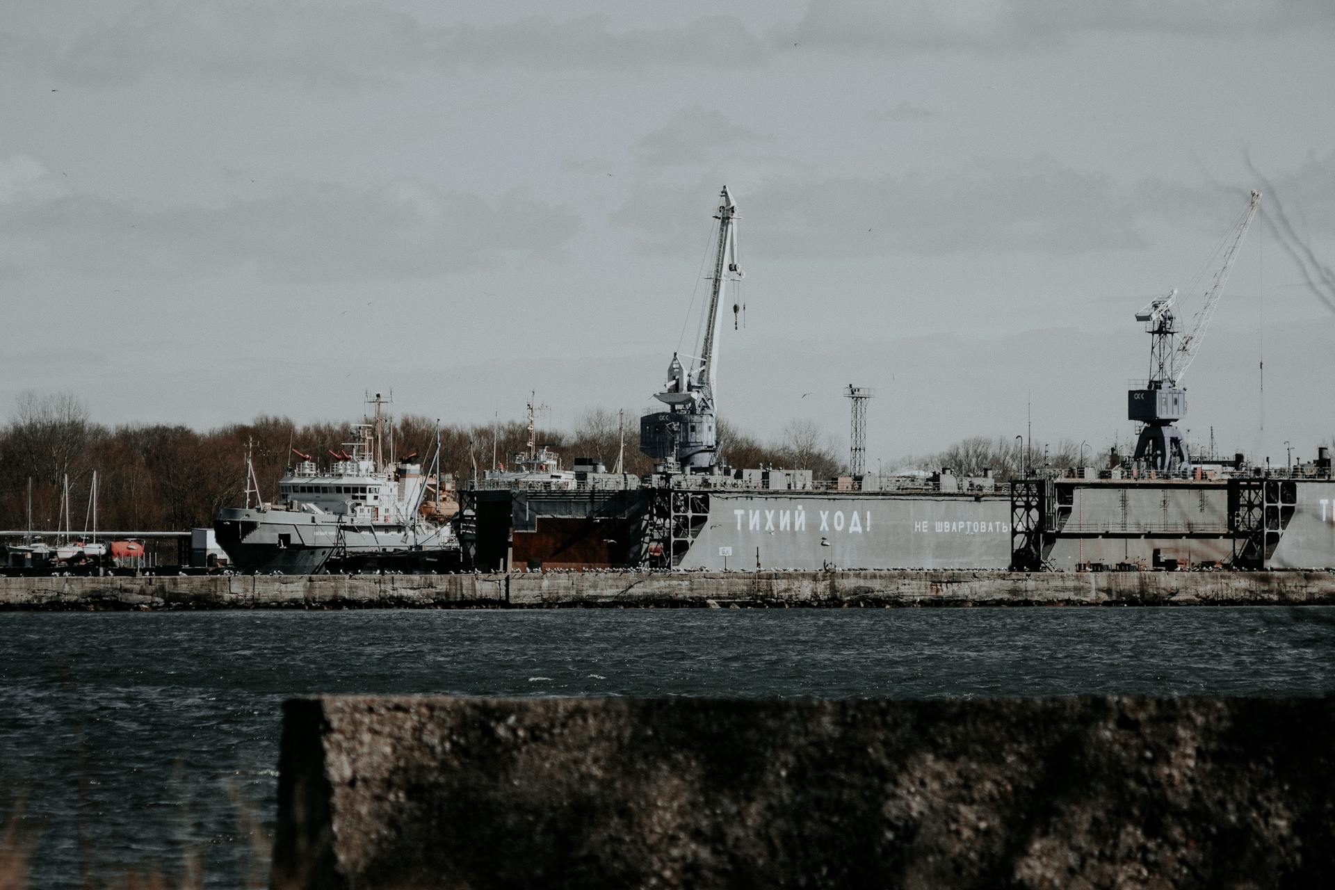 A shipyard with cranes and ships in a harbor under a cloudy sky.