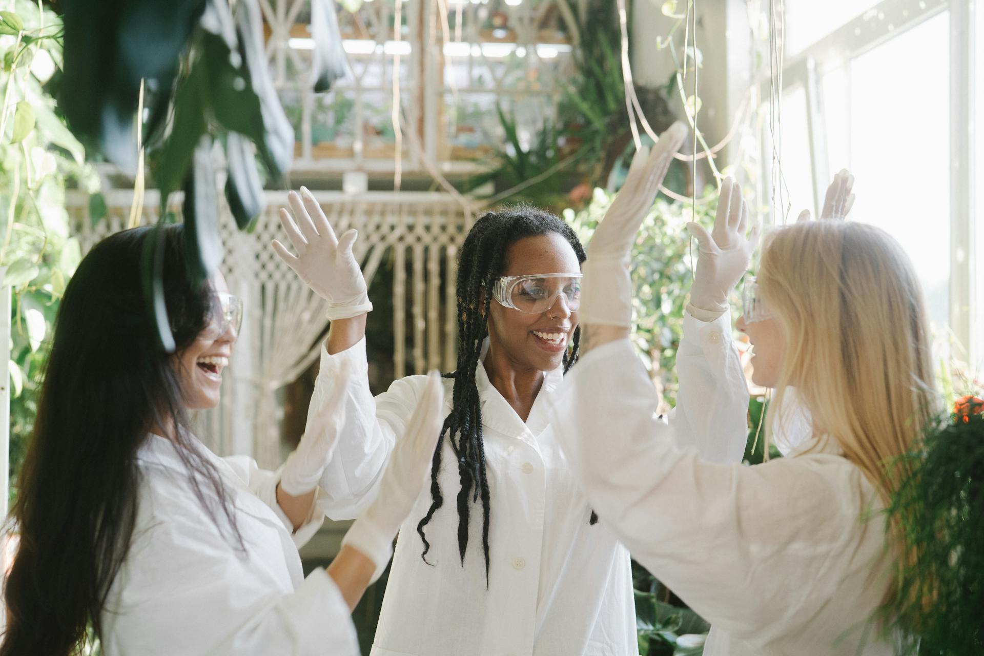 Women Wearing Laboratory Gowns Doing High Five while Facing Each Other