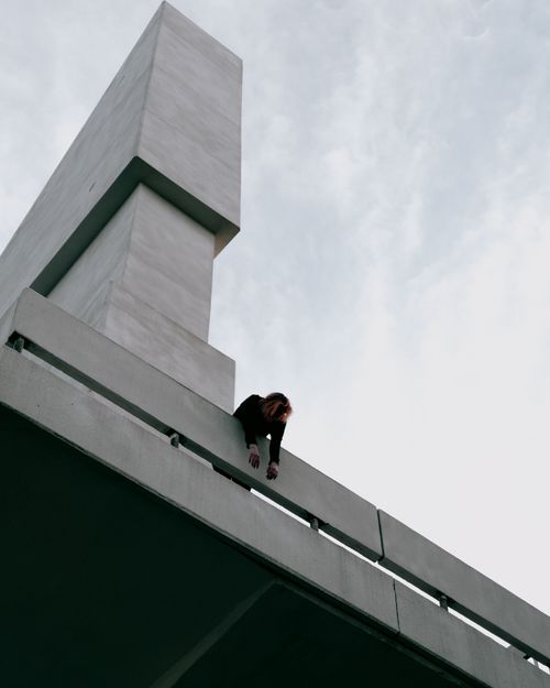 Free A person leaning over a modern concrete structure under a white sky, showcasing urban architecture. Stock Photo