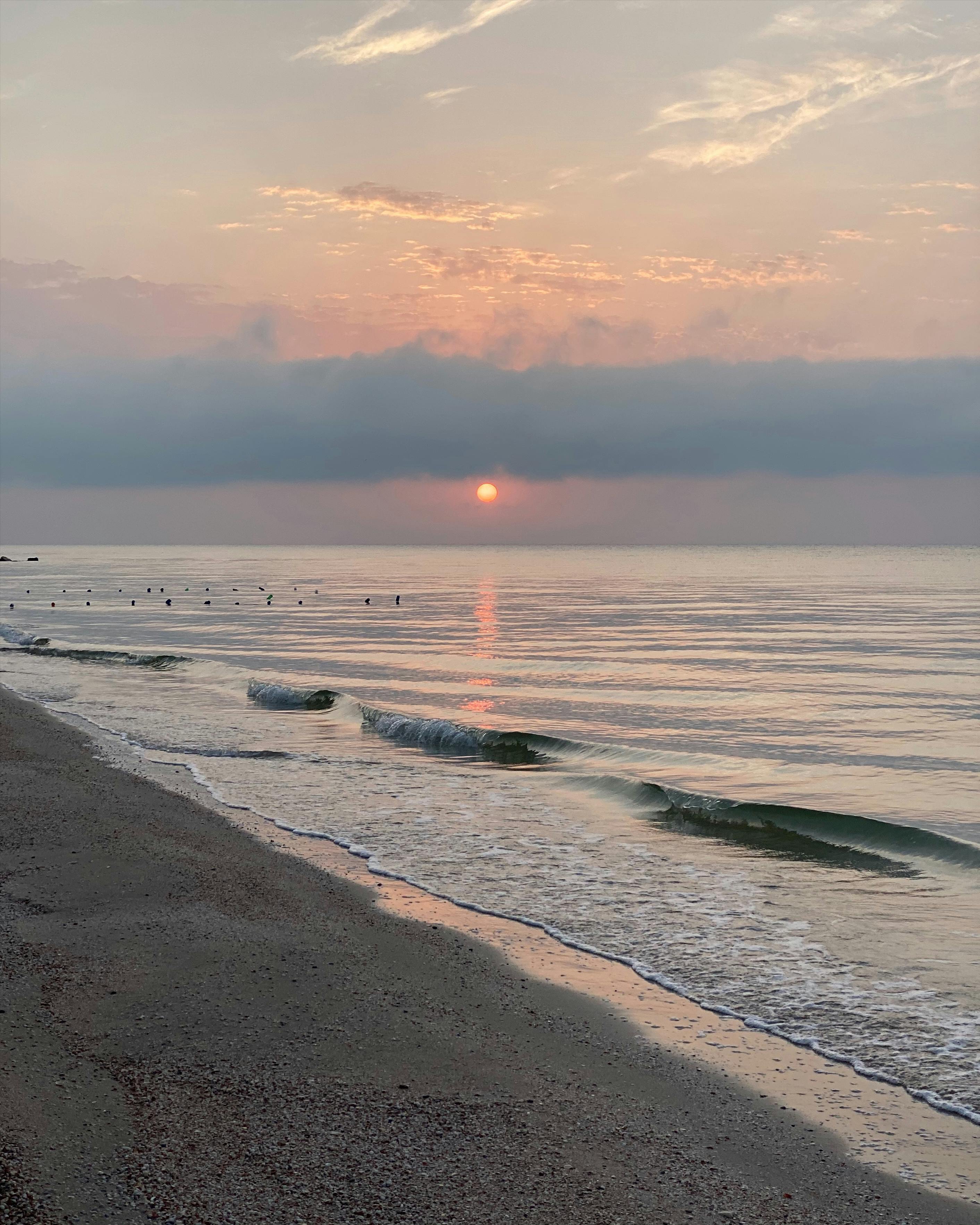 A peaceful sunset over calm waves on a sandy beach with cirrus clouds.