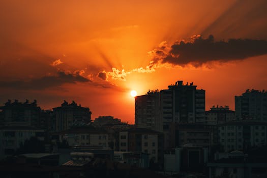 Stunning sunset over city skyline with vibrant orange skies and silhouetted buildings.