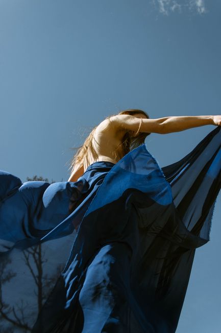 A model in a flowing blue dress poses gracefully against a clear sky.