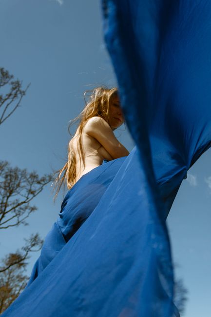 A creative outdoor photoshoot featuring a woman wrapped in blue fabric, exuding freedom and elegance.