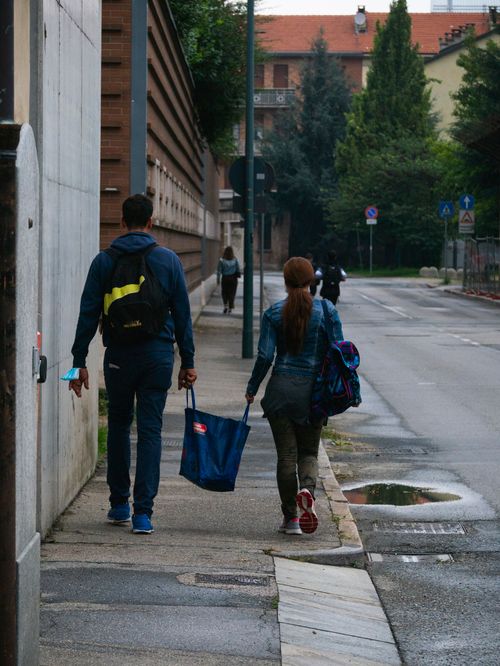 Free Back view of a couple with bags walking on an urban sidewalk in casual attire. Stock Photo