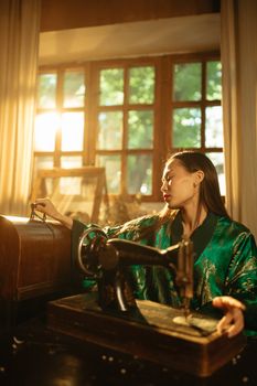 Elegant Asian woman wearing a kimono working with a vintage sewing machine near a sunlit window.