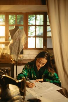 Japanese woman working on fashion designs in atelier with natural lighting.