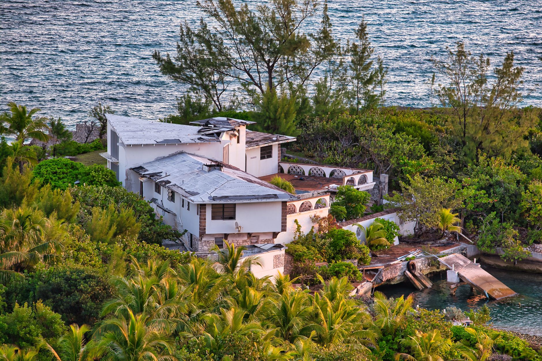 Aerial view of a weathered villa surrounded by lush greenery on the Bahamian coast.