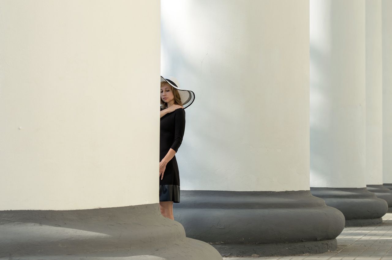 a stylish young woman in a black dress and sun hat stands beside white