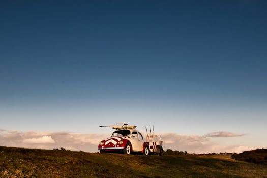A vintage car parked on a grassy hill with surfboards under a clear blue sky in Hamburg.