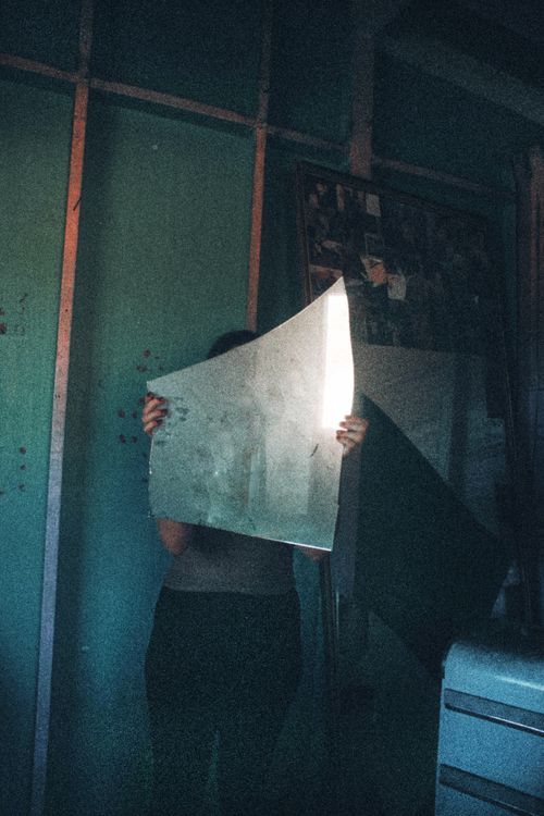 Free A person holding a shard of mirror reflecting light in a dimly lit room, creating a mysterious atmosphere. Stock Photo