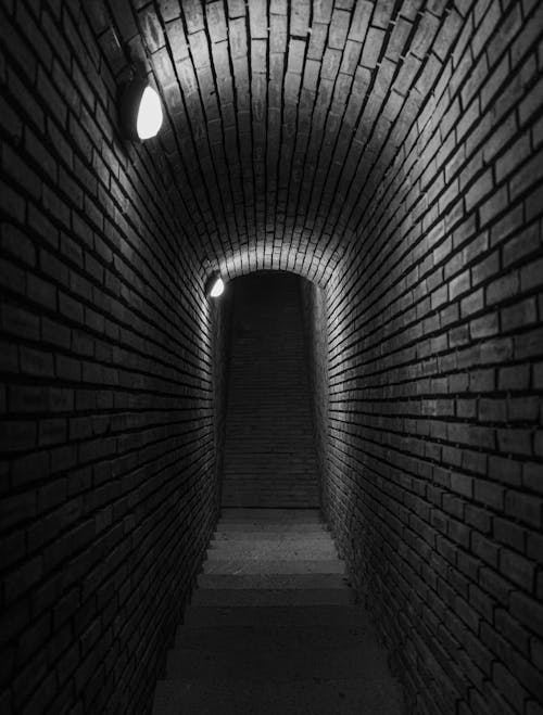 Grayscale Photo of Brick Wall Tunnel
