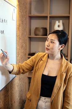Asian woman presenting ideas on whiteboard during business meeting, promoting creative teamwork.