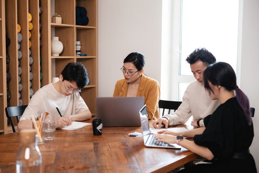 A diverse group of professionals working together around a table with laptops in a modern office.