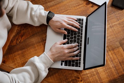 Free Close-up of hands typing on a laptop at a wooden desk, showcasing casual work setup. Stock Photo