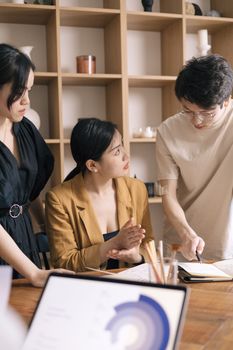 Three colleagues engaged in a collaborative meeting in a modern office setting, discussing plans and ideas.