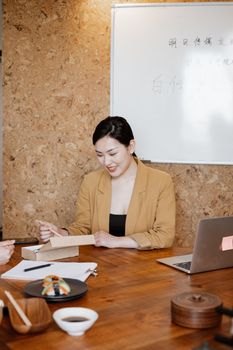 Young professional woman at a wooden table working with documents and a laptop, smiling in an office setting.