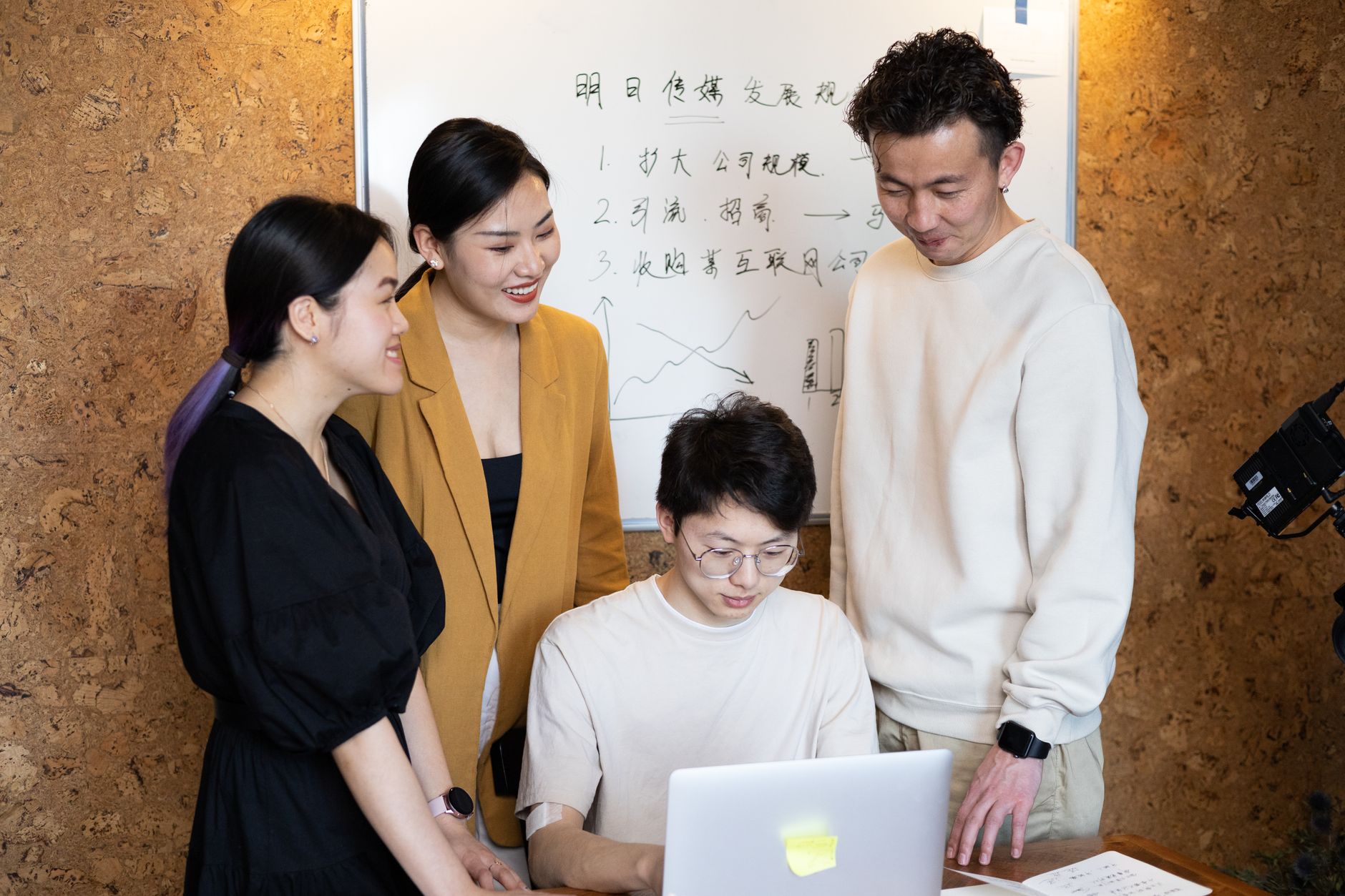 Four colleagues in a bright office environment, working on a project together with a laptop.