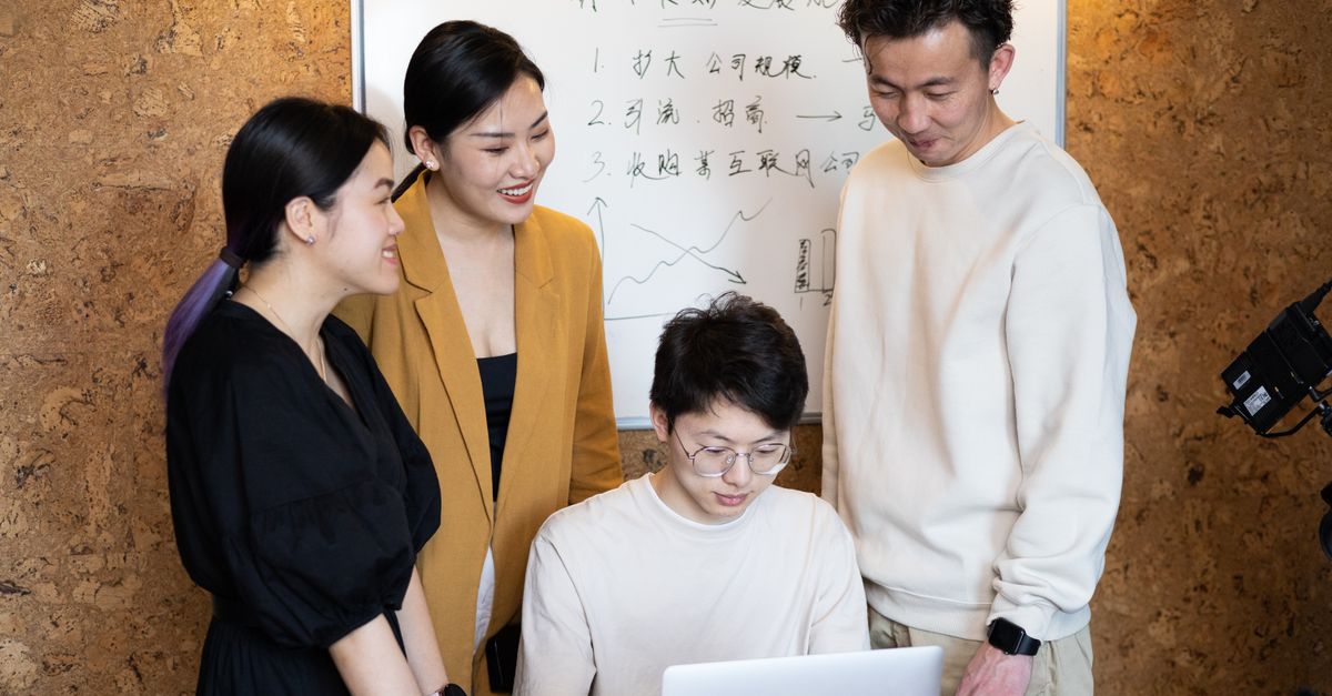 diverse group of young professionals collaborating in a modern co-working space with laptops and whiteboards