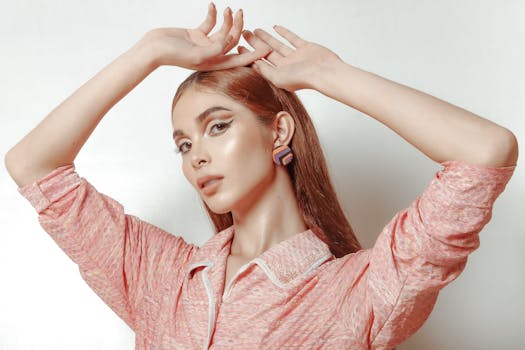 Portrait of a young woman posing gracefully with hands on head, wearing a pink outfit.