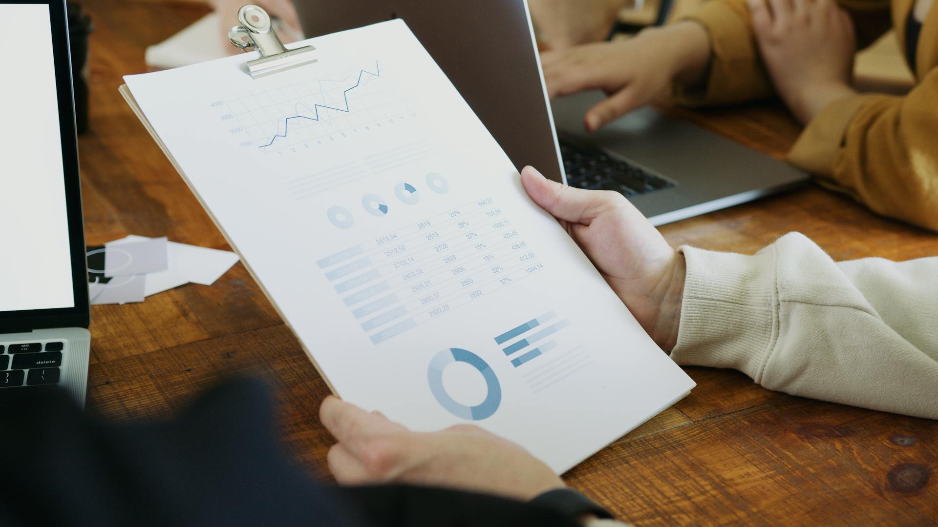 Close-up of hands holding a clipboard with charts and graphs in a business meeting.