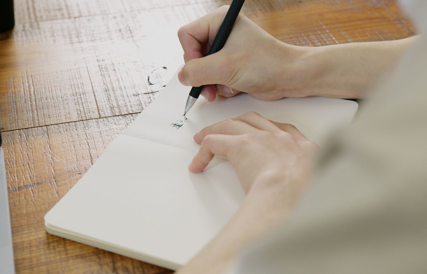 Close-up of hands writing in a notebook with a pen on a rustic wooden table.