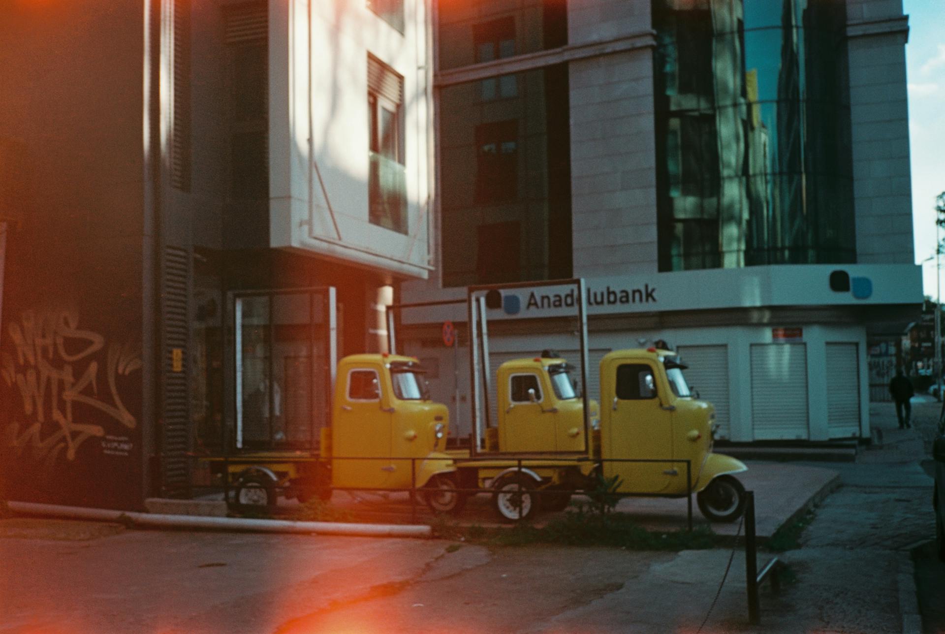 Three yellow trucks parked beside a modern building in an urban area.