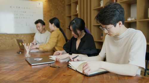 Free Group of diverse students studying at a wooden table in a modern classroom with laptops and notebooks. Stock Photo