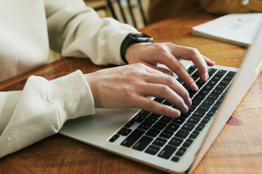 Hands typing on a laptop keyboard on a wooden desk, close-up view.