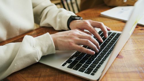 Free Hands typing on a laptop keyboard on a wooden desk, close-up view. Stock Photo