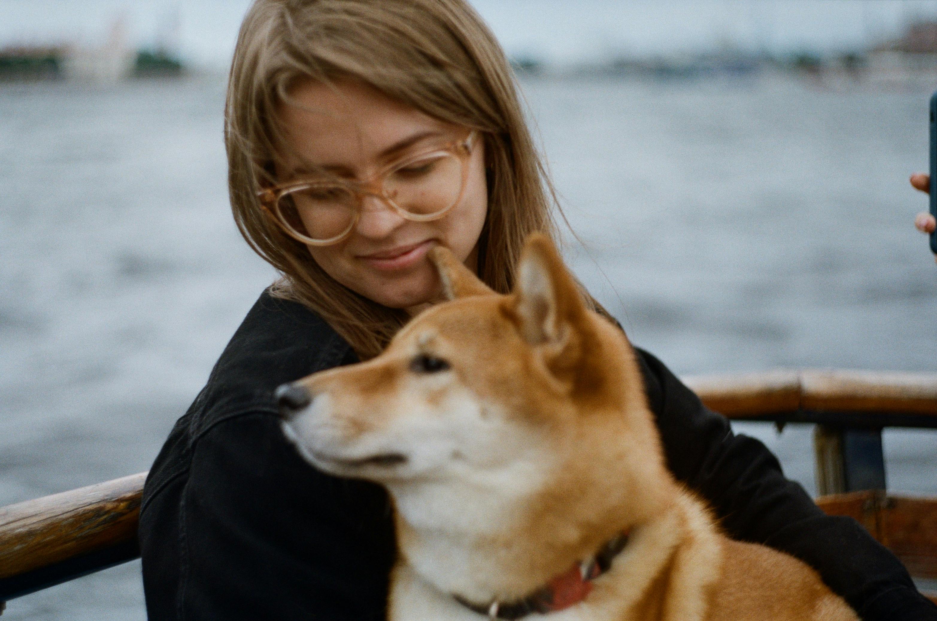 A woman with eyeglasses hugging her Shiba Inu on a boat trip outdoors.