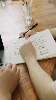 Two people taking notes together on an open notebook placed on a wooden table.