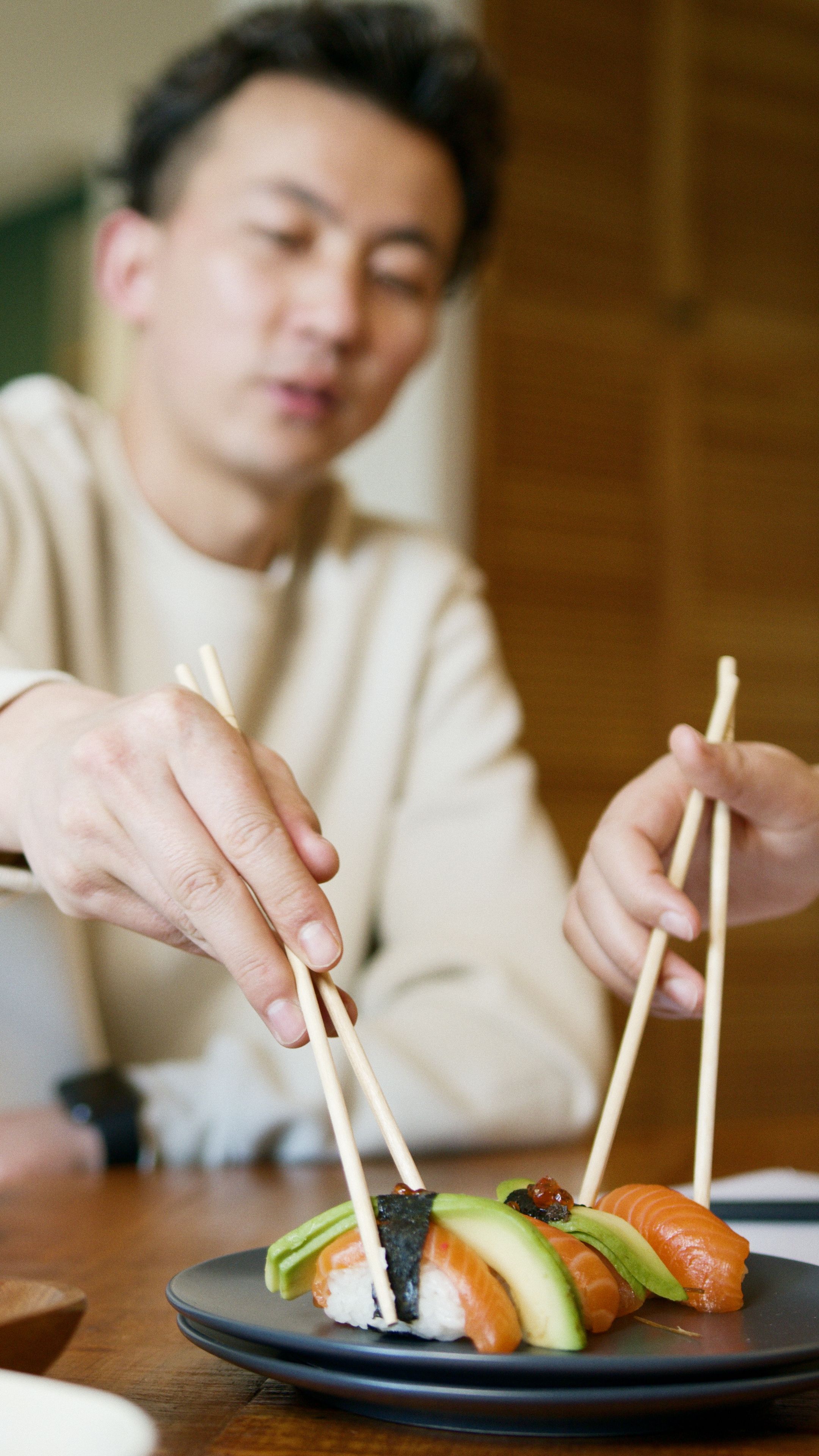 Two people share a plate of nigiri sushi using chopsticks at a Japanese restaurant.