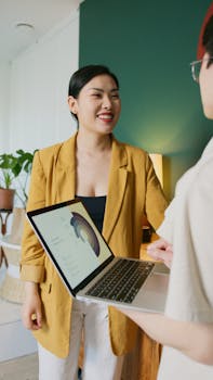 Asian woman smiling during a business meeting indoors, holding a laptop with a colleague.