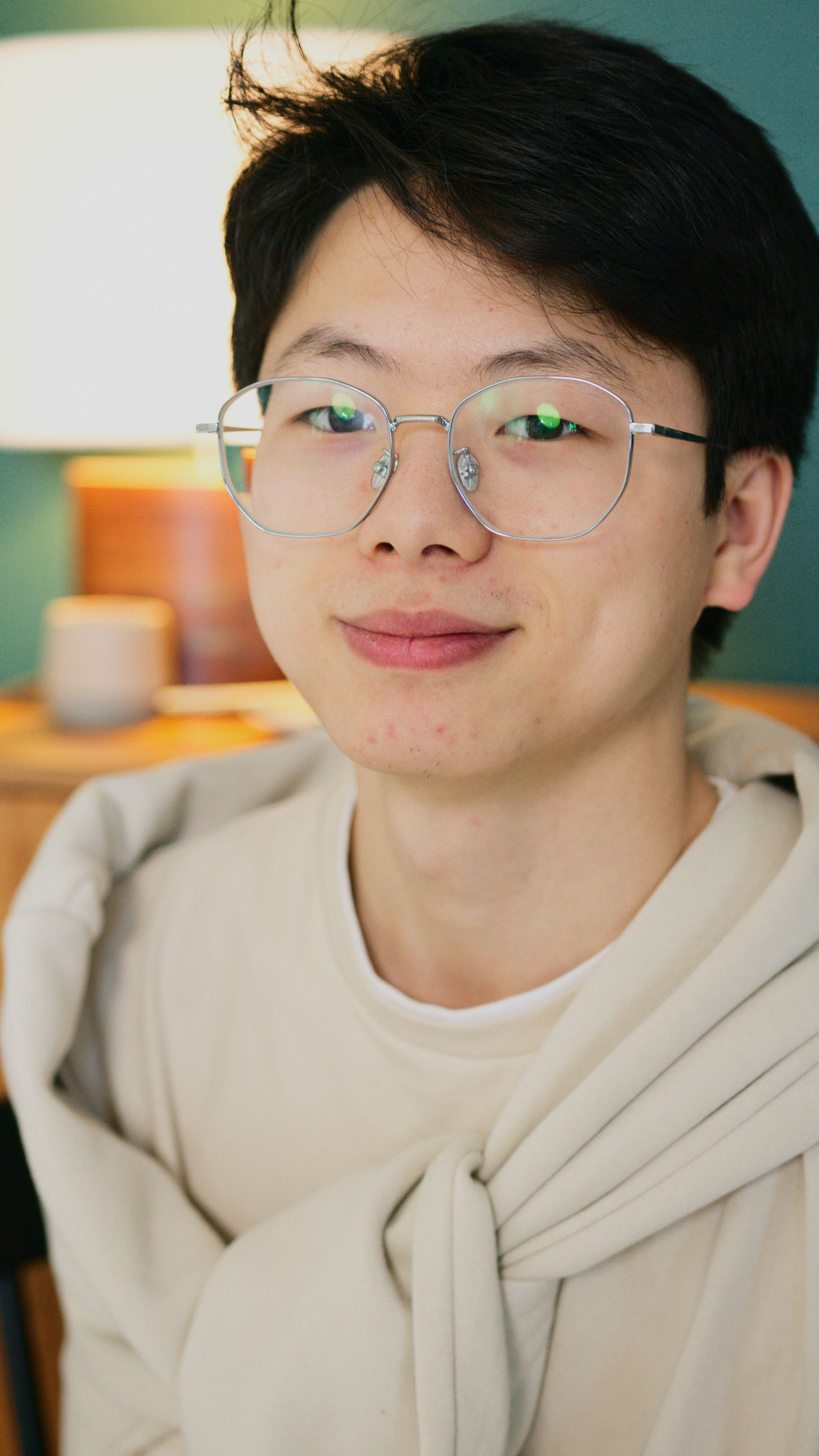 Close-up portrait of a smiling young man wearing glasses and a cozy sweater indoors.