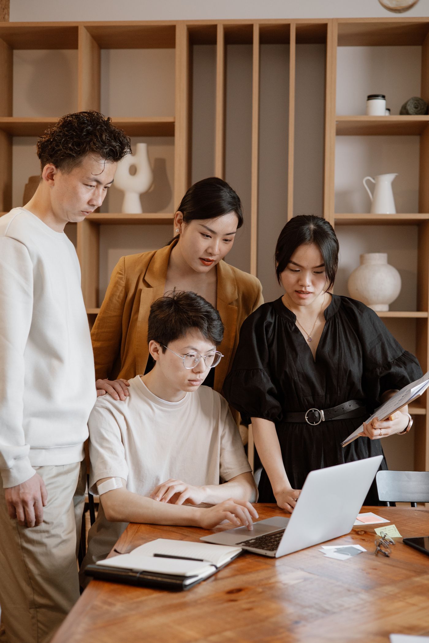 Asian business professionals discussing strategy around a laptop in a modern office
