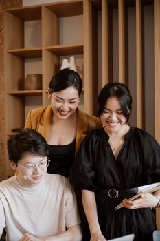 Three Asian colleagues collaborate happily in a modern office setting, promoting teamwork and a positive work environment.