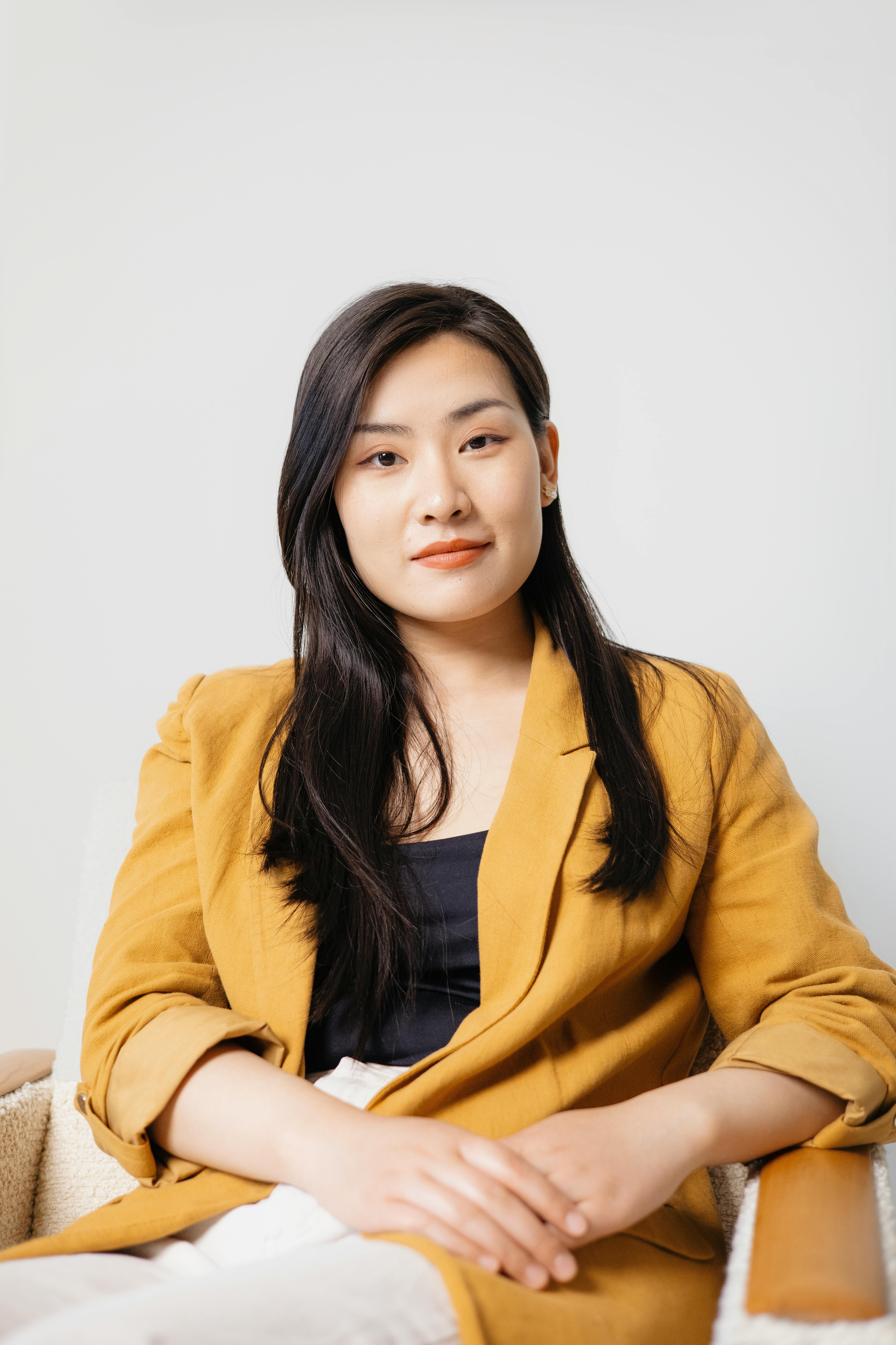 Portrait of a confident young businesswoman in a yellow blazer sitting indoors.