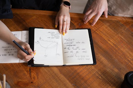 Overhead view of hands discussing and taking notes on a notebook during a collaborative session.